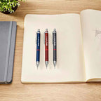 Three Rotring Tikky Retro 0.7mm Mechanical Pencil in 3 colours on an open notebook with a wooden surface and plant in the background