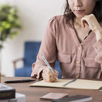 Woman in a pink blouse writing with Rotring 600 3-in-1 Multi Pen with Mechanical Pencil in Silver in a notebook at a desk with a blurred background