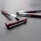 Two pens with burgundy and silver accents on a gray surface
