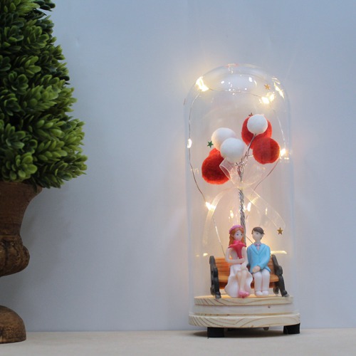 Couple Sitting On Bench With Balloons And Lights In Glass Shape Dome Showpiece